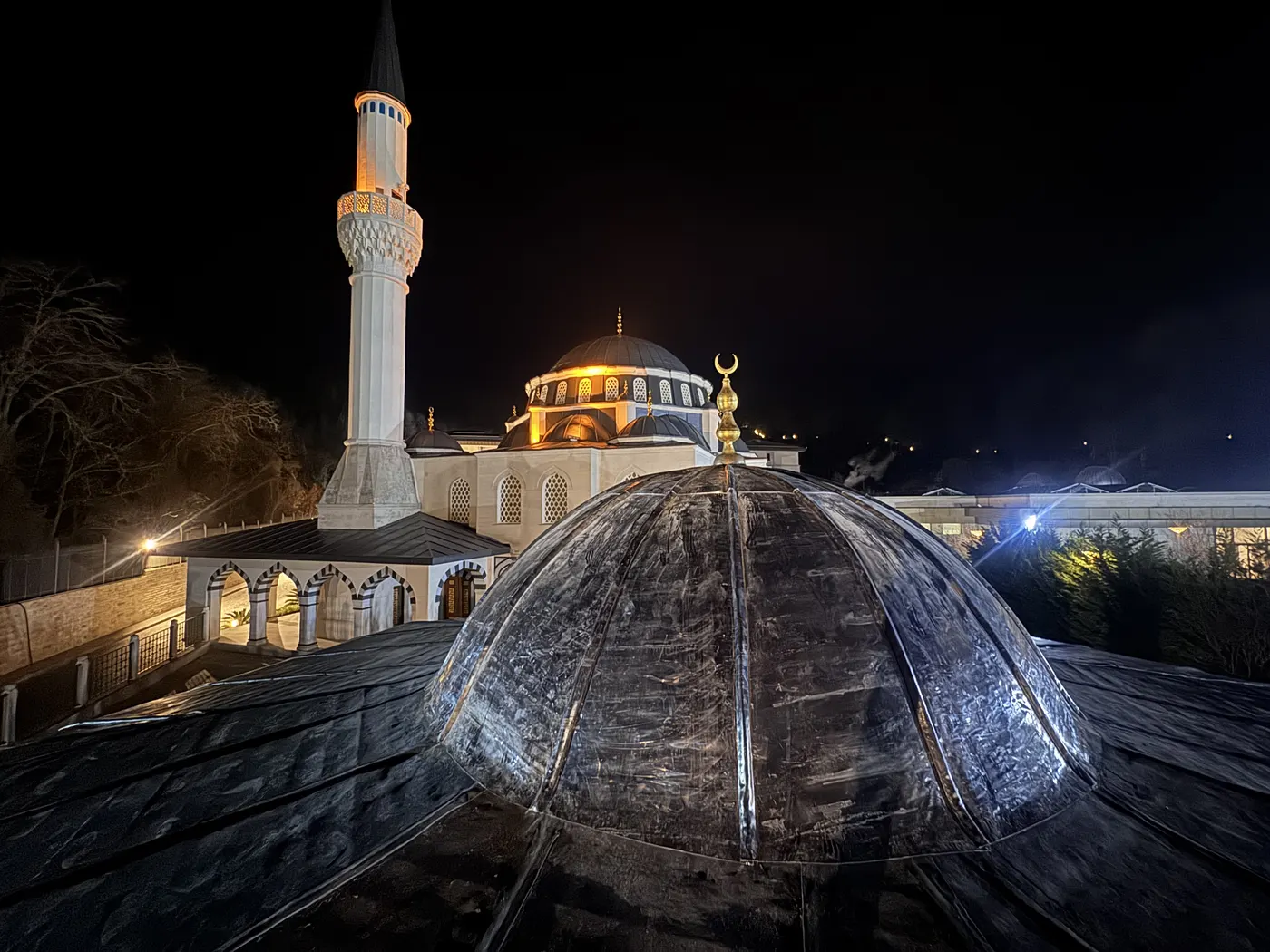 Gece aydınlatmalı cami kubbesi üzerinde tamamlanmış kurşun kaplama uygulaması, arkada minare